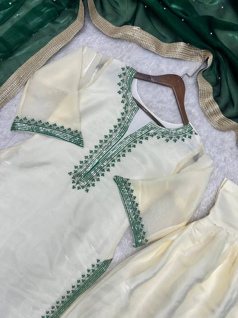 Cream-colored traditional kurta set with green embroidered borders, displayed on a hanger with a matching green dupatta featuring a gold border.