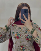 A woman taking a mirror selfie wearing a beige floral printed salwar kameez top with green and gold embroidery, a deep red dupatta, and green beaded bangles.