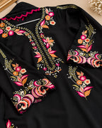 A black long-sleeve tunic or kaftan with elaborate floral and paisley embroidery in pink, orange, gold, and white, shown in a close-up flat-lay view.