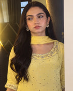 A woman with long dark hair wearing a yellow embellished kurta with a matching dupatta and silver-toned earrings, shown in an indoor setting.