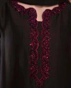 Close-up of a black garment with ornate magenta embroidery and sequin embellishment around a keyhole neckline.