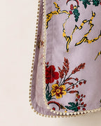 Close-up of a lavender fabric item with a colorful floral print in red, yellow, and green, finished with a decorative cream pom-pom trim.