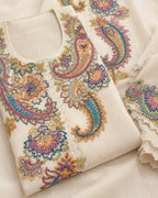 A folded cream-colored fabric garment featuring intricate multicolor paisley and floral embroidery in pink, blue, gold, and green, with a scalloped lace-trimmed sleeve visible on the right.