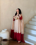 A woman wearing a traditional Indian salwar kameez outfit in beige and deep red, standing next to white stairs in a rustic indoor setting.