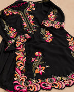 A black embroidered tunic or kurta laid flat on a beige background, featuring vibrant floral and paisley embroidery in pink, orange, yellow, and green.