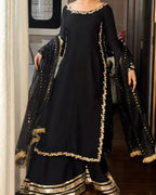 A black traditional Anarkali suit with gold floral embroidery and striped borders, paired with a matching sheer black dupatta, shown on a model in an indoor setting.