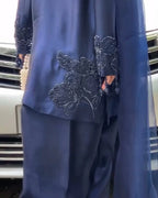 A close-up of a navy blue traditional outfit with intricate silver beaded floral embroidery on the sleeves and lower tunic, worn by a model standing in front of a car.