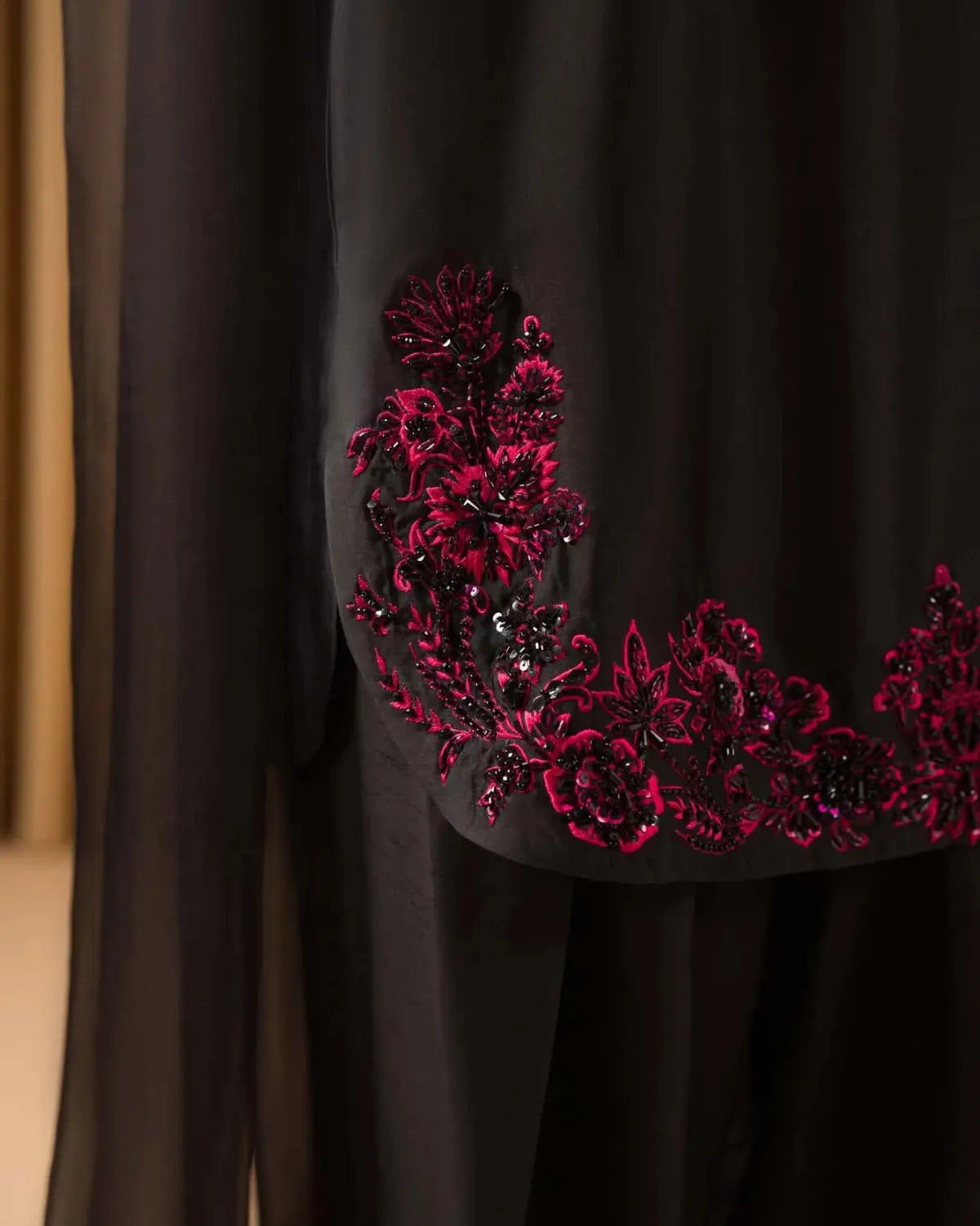 A close-up of a black garment featuring a prominent, ornate magenta and black floral embroidered applique along the hem.