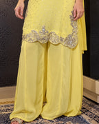 A close-up of a person wearing a bright yellow traditional outfit with wide flowing pants, a matching draped fabric, and ornate silver embroidery along the hem.