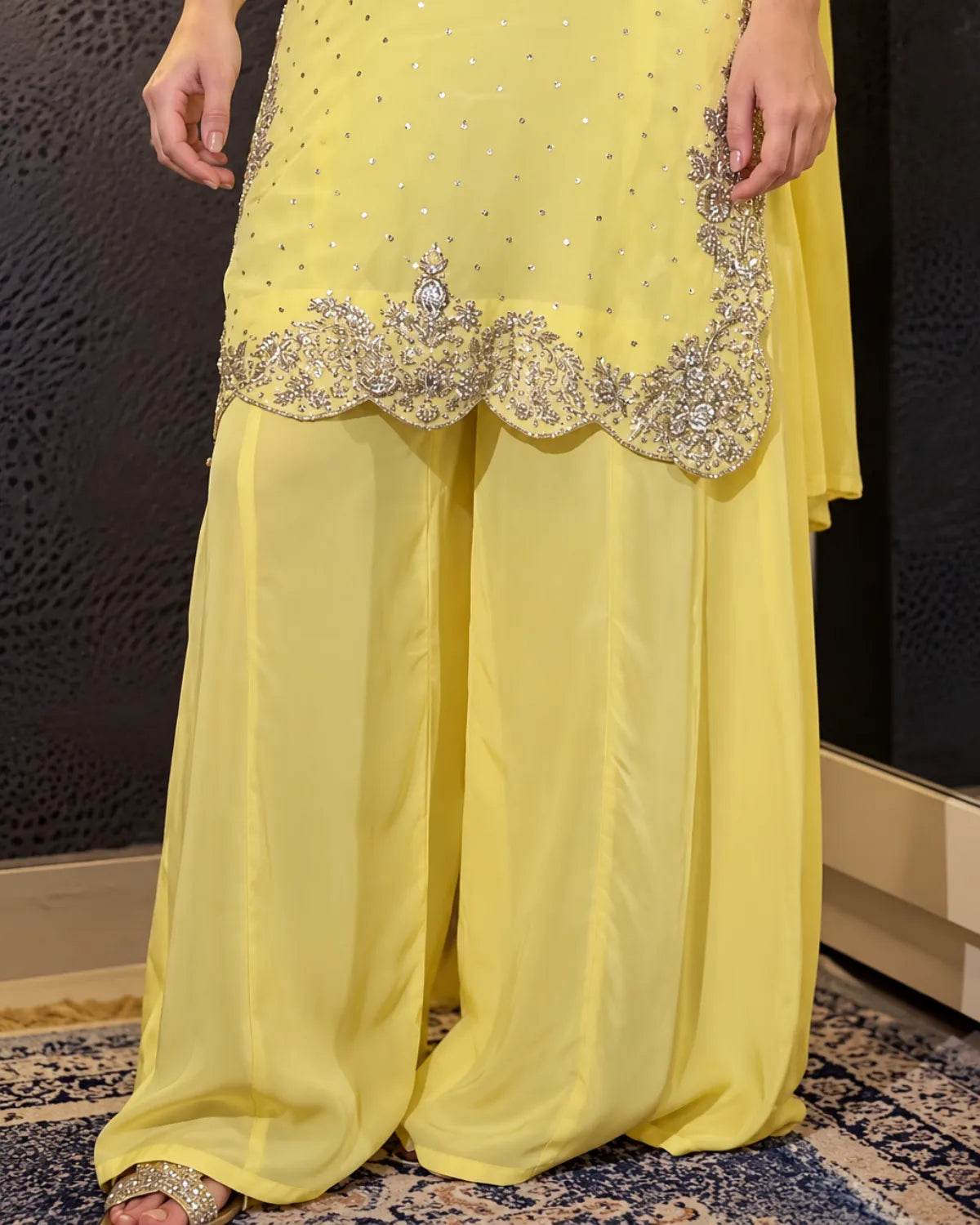A close-up of a person wearing a bright yellow traditional outfit with wide flowing pants, a matching draped fabric, and ornate silver embroidery along the hem.