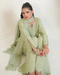 A woman wearing a sage green traditional outfit with a matching scarf, seated against a plain white background.