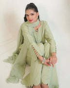 A woman wearing a sage green traditional outfit with a matching scarf, seated against a plain white background.