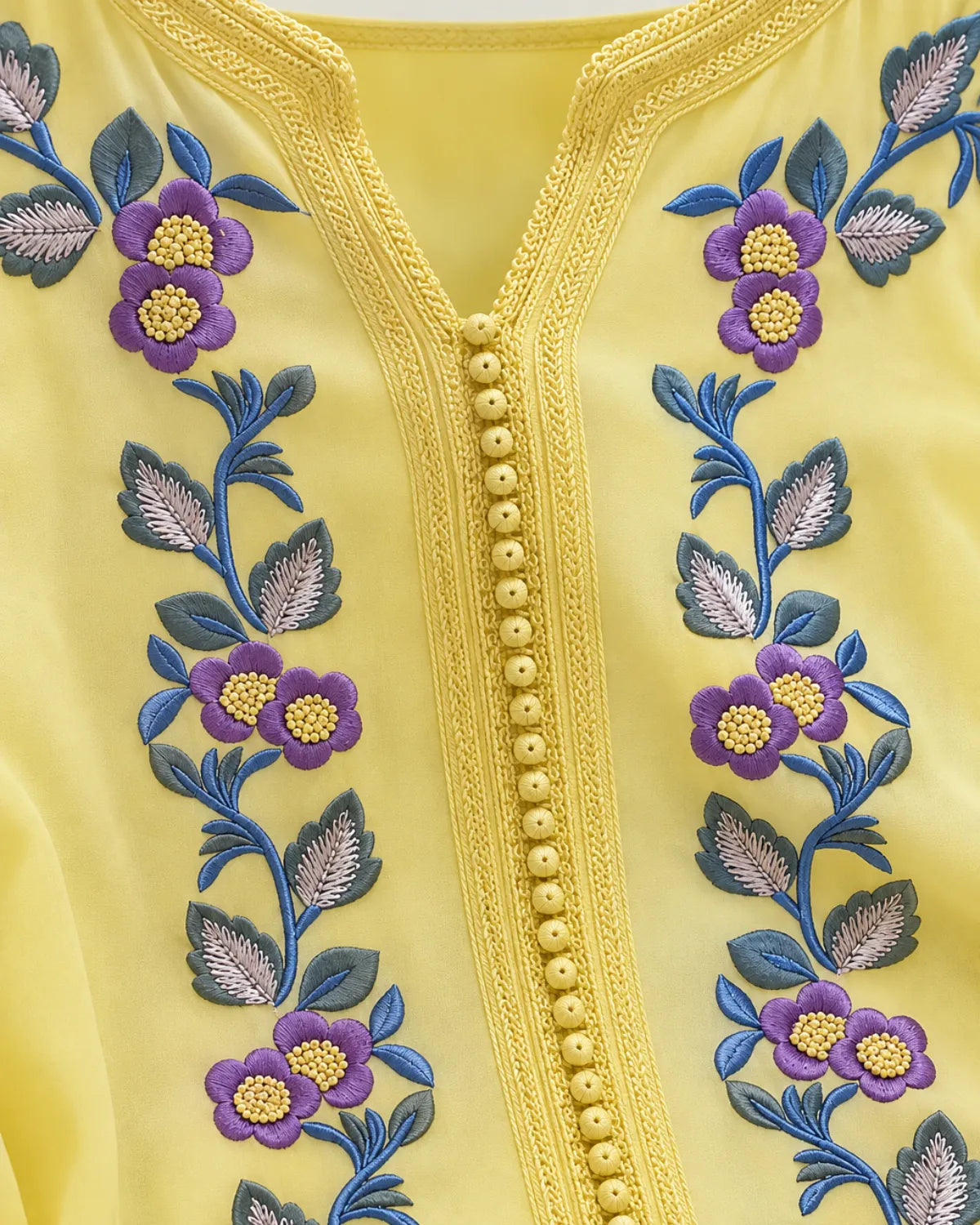 Close-up of a yellow embroidered garment featuring purple flowers, blue and silver leaves, and a decorative beaded neckline.