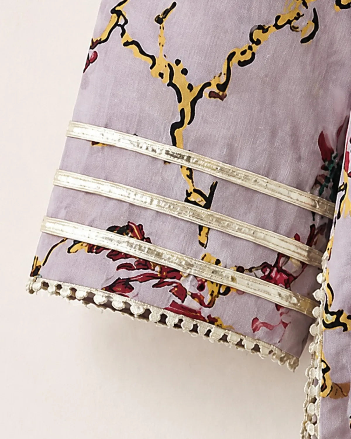 Close-up of a lavender printed fabric sleeve with yellow and red floral branch motifs and three horizontal silver metallic bands near the cuff.