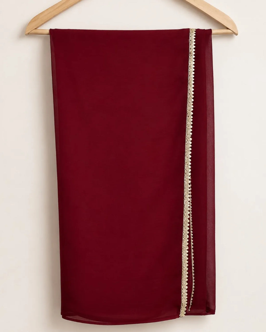 A deep burgundy red scarf draped over a wooden hanger against a plain off-white background, featuring a decorative cream-colored beaded border along one side.