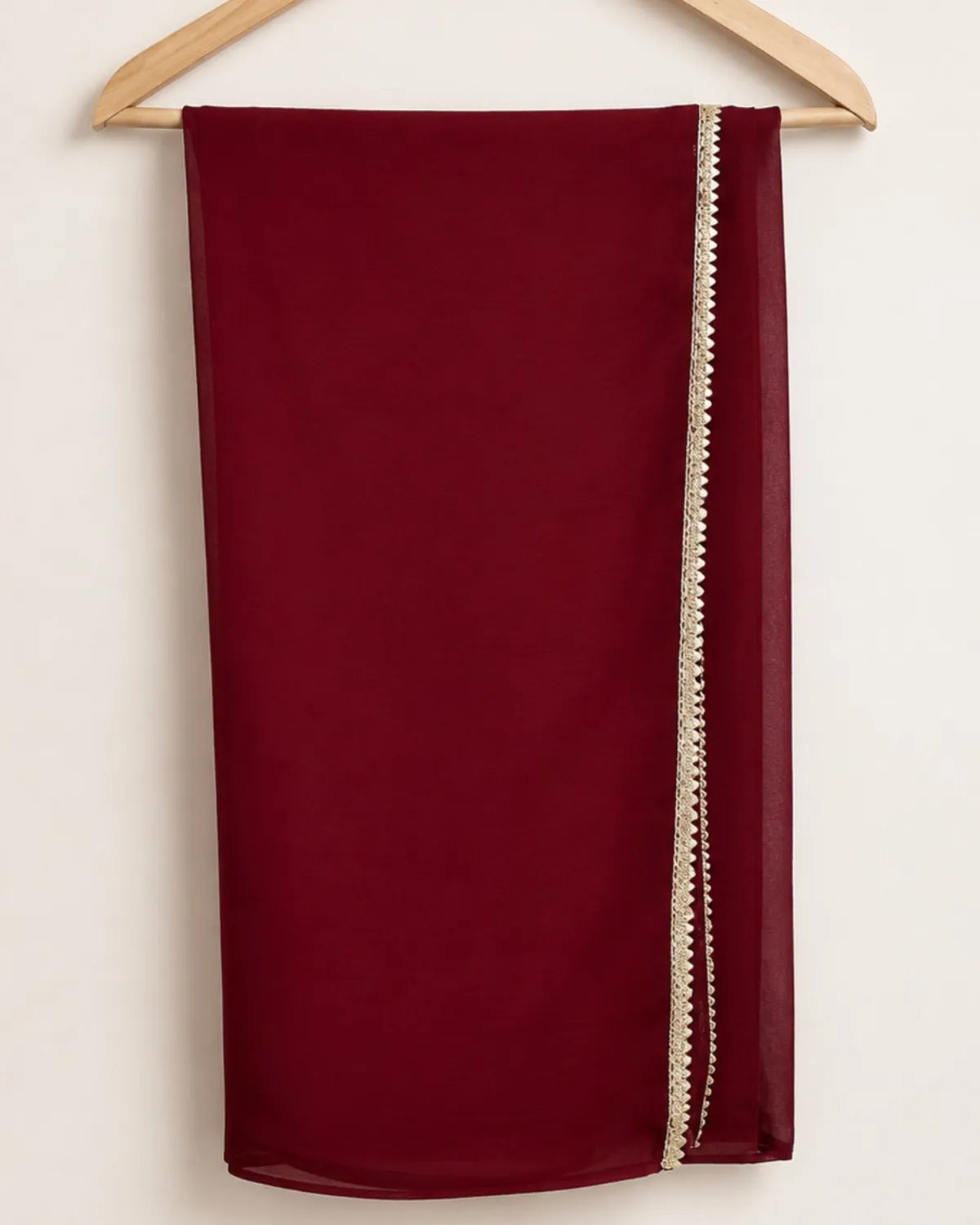 A deep burgundy red scarf draped over a wooden hanger against a plain off-white background, featuring a decorative cream-colored beaded border along one side.