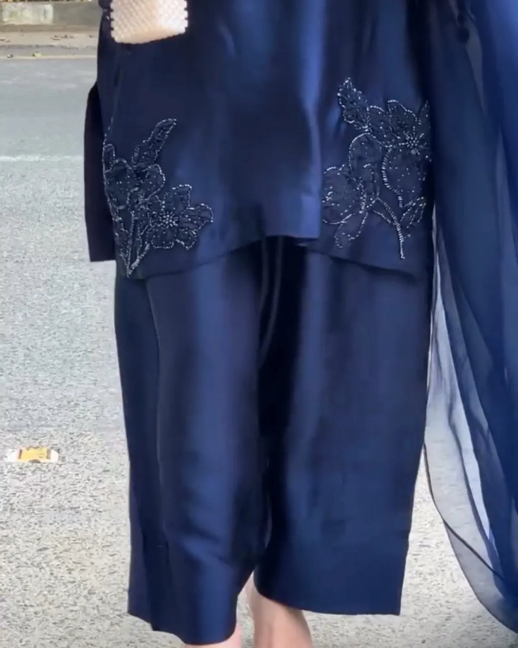 A close-up of a navy blue traditional outfit with floral embroidered details on the sleeves, worn by a person standing outdoors on a paved surface.