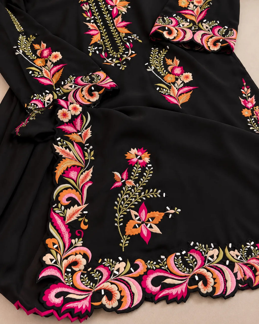 Black embroidered fabric garment with vibrant floral and paisley embroidery in pink, orange, yellow, and green, shown in a close-up flat lay.