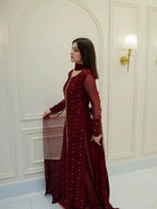 A woman wearing a deep maroon long gown with silver embellishments, standing in a white paneled room.